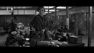 Ein Filmstill von "The Apartment" des Regisseurs Billy Wilder von 1960 zeigt die Chefsekretärin Miss Olsen, hinter der zwei Monsterae deliciosae prangen.