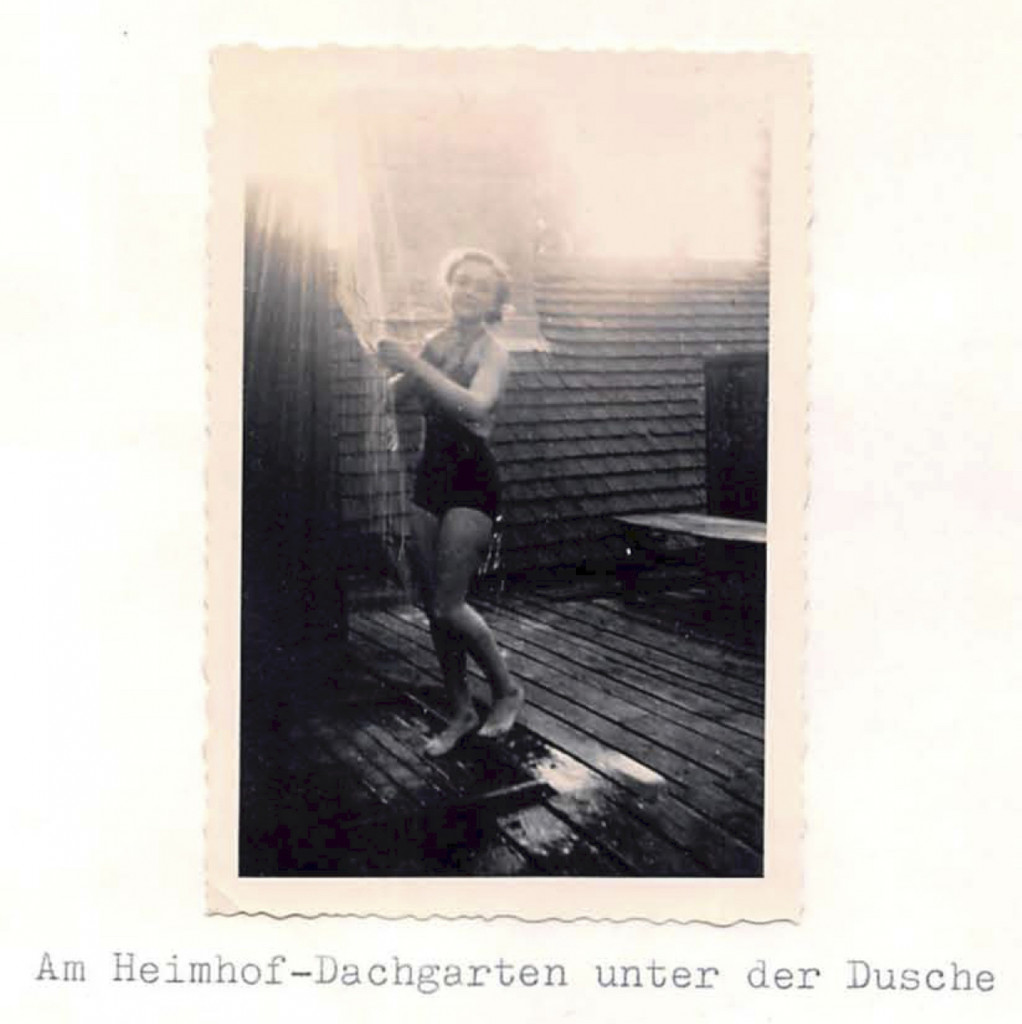 Foto einer jungen Frau im Badeanzug unter einer Dusche auf einer Dachterrasse.